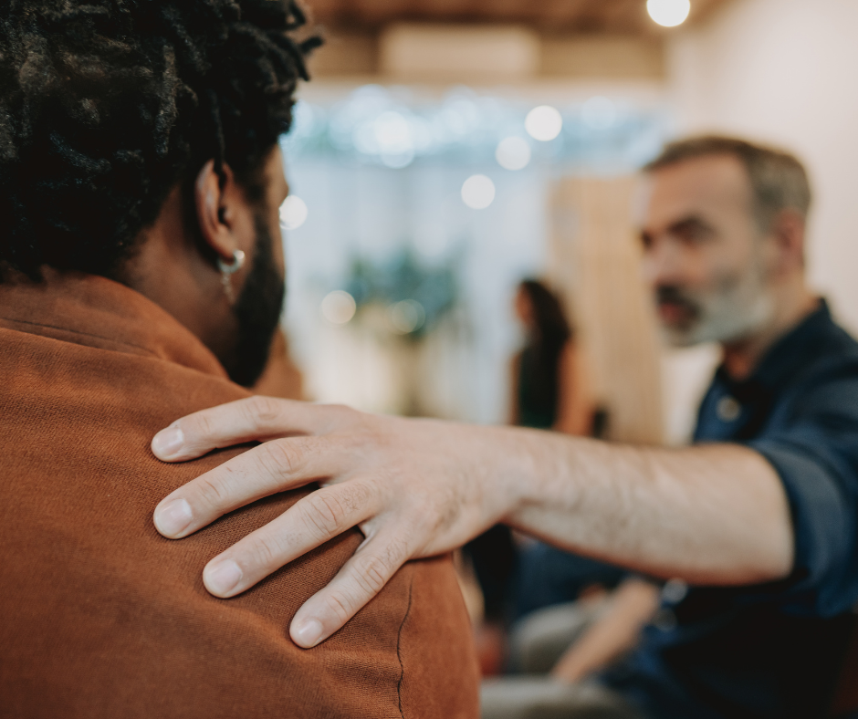 A person comforts a grieving friend with a supportive hand on their shoulder, highlighting compassion, connection, and ongoing grief support.