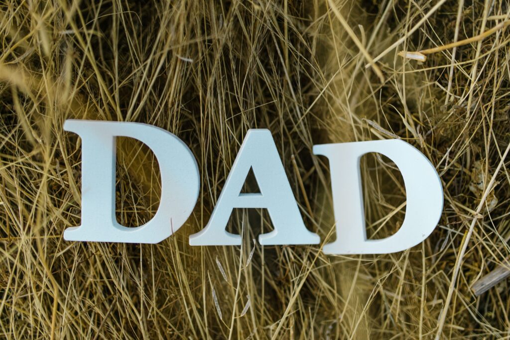 Decorative letters spelling "DAD" displayed among tall golden grass, symbolizing remembrance, love, and the enduring legacy of fathers who have passed away. The image reflects themes of Father's Day remembrance, family memories, and honoring the impact fathers leave on future generations.
