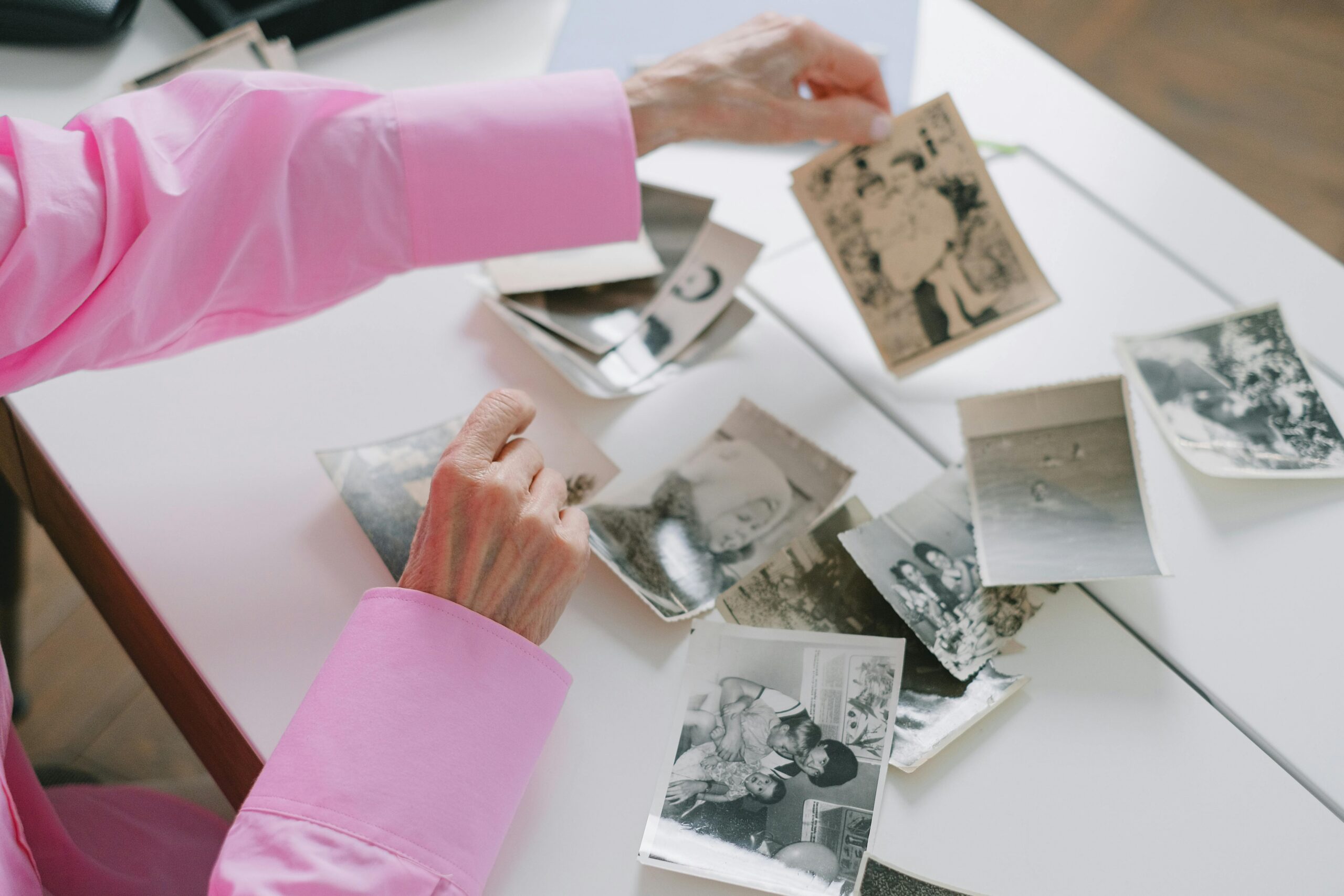 Person sorting through cherished family photographs at a table, reflecting on memories and personal stories. The image represents meaningful remembrance and creating a heartfelt funeral or memorial service that focuses on honoring a loved one's life rather than the cost of arrangements.
